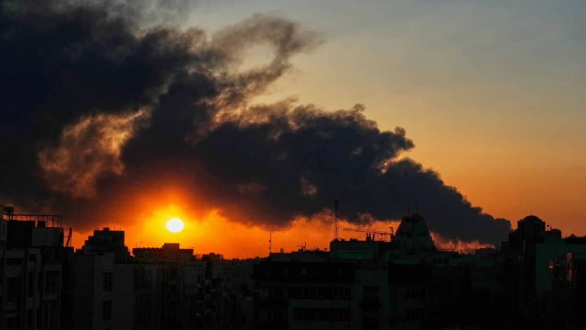 The sun sets behind a plume of smoke rising after a U.S.–Israeli military strike in Tehran, Iran