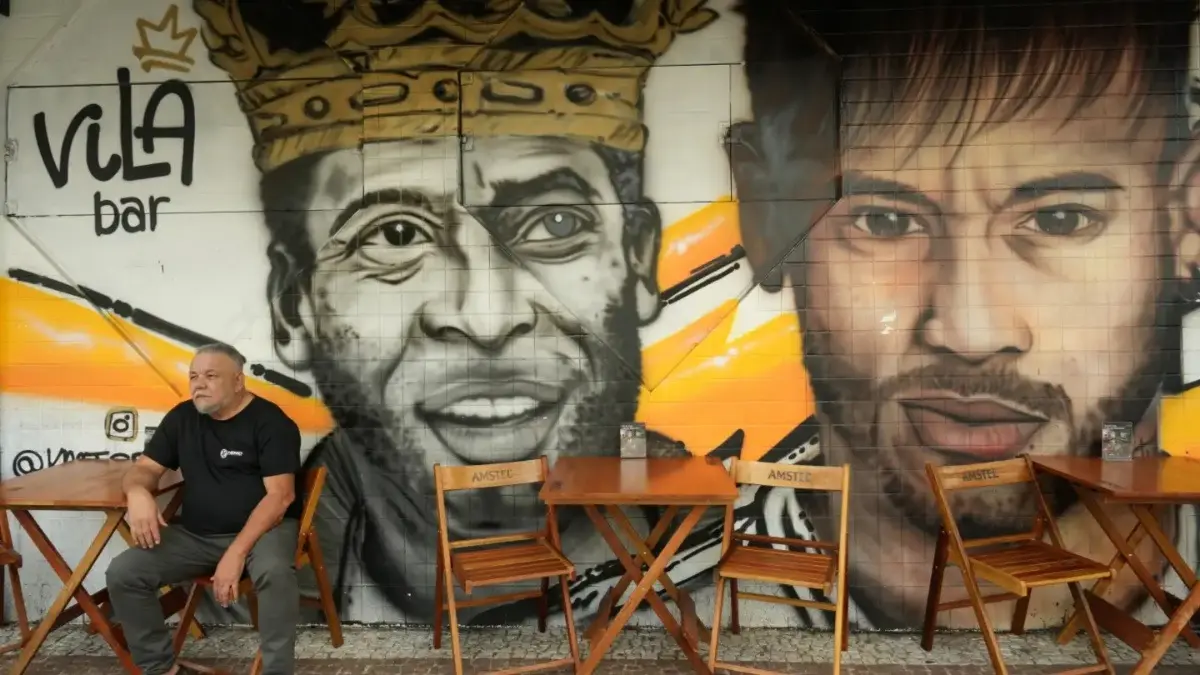 Football Great Pelé’s Legacy Shines On In Brazil Ahead Of FIFA World Cup 2026 A man sits in front of a mural of Pele and Neymar in Santos, Brazil
