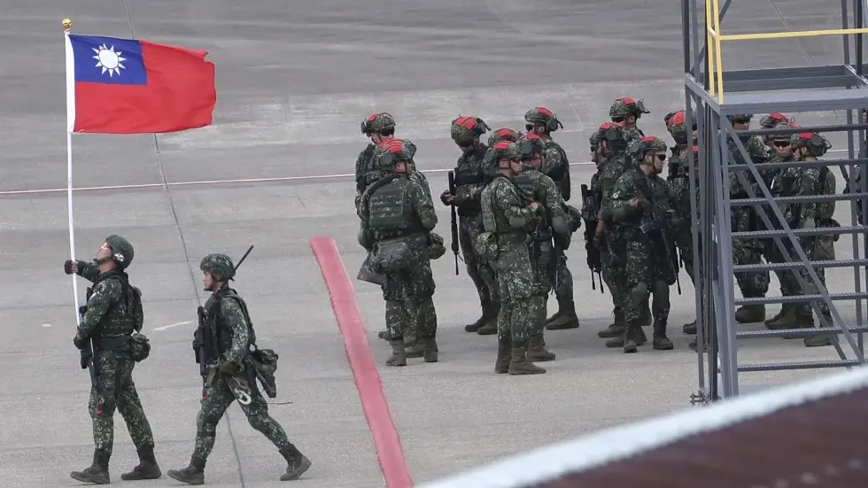 A Taiwanese soldier holds a Taiwan national flag near a group of soldiers with red markings on their helmet