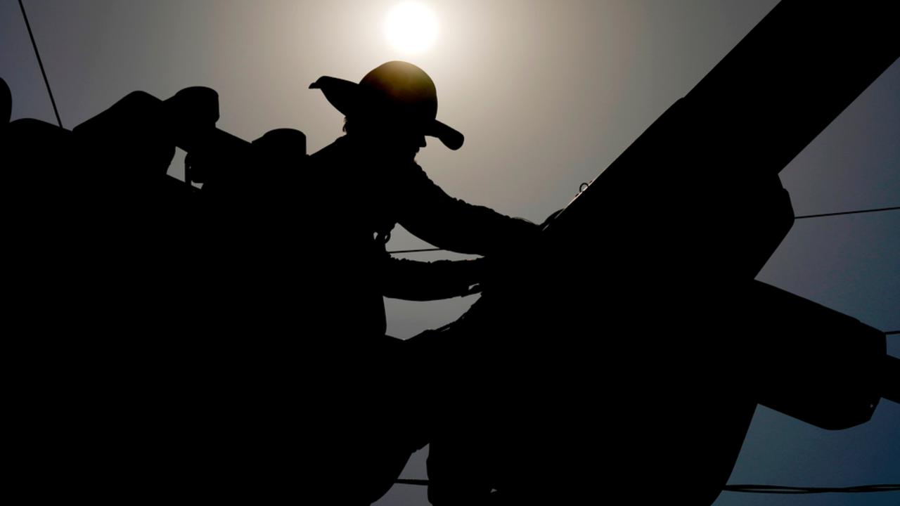 A linesman works on power lines under the morning sun