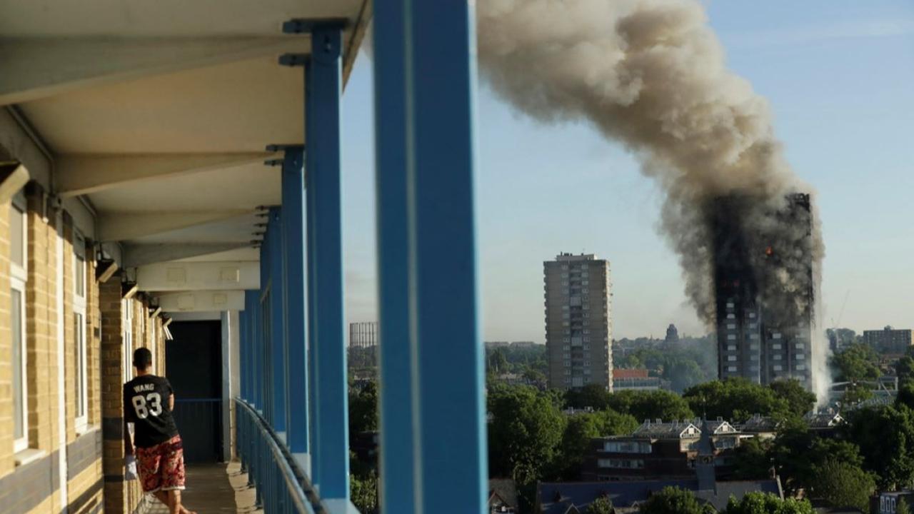 A resident in a nearby building watches smoke rise from the Grenfell Tower building on fire in London