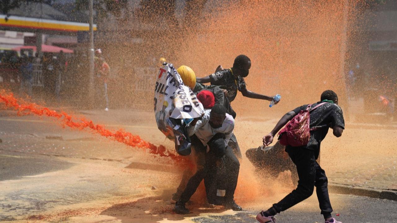 Protesters scatter as Kenya police spray water canon at them during a protest over proposed tax hikes in a finance bill in downtown Nairobi