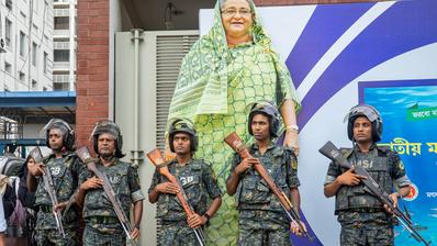 Military personnel stand guard in front of a large cutout portrait of Prime Minister Sheikh Hasina