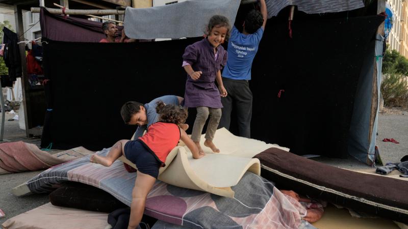 Children play as their father, left, set up a tent as temporary shelter after fleeing the Israeli airstrikes in Beirut, Lebanon