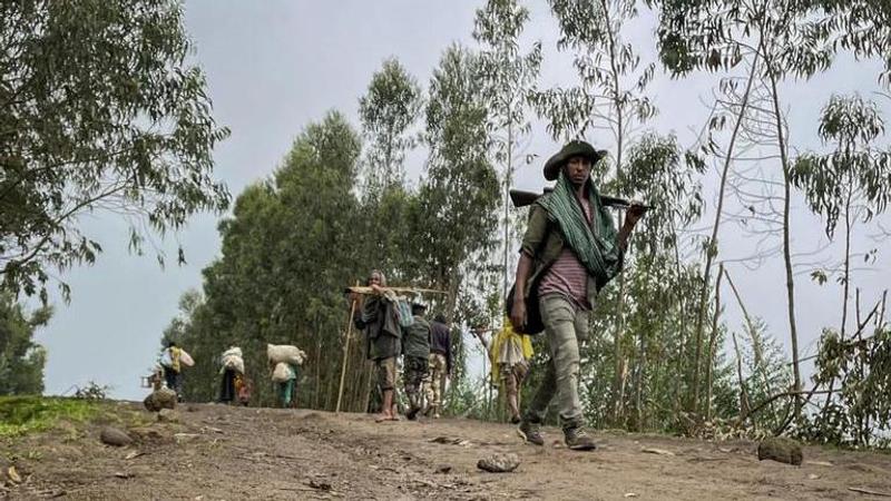 An unidentified armed militia fighter walks down a path as villagers flee with their belongings in the other direction, near the village of Chenna Te