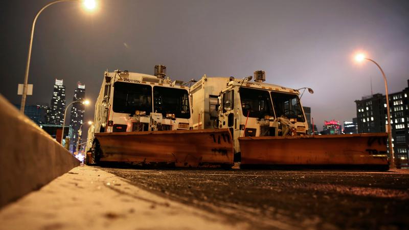 Sanitation trucks mounted with snow plows are parked on the west side of Manhattan in New York