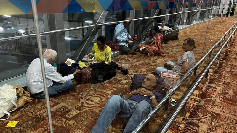 Distressed Air India passengers can be seen sitting, eating and lying on the floor of Delhi Airport as they wait to board their flight