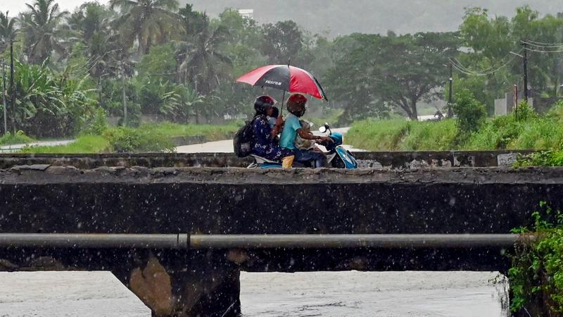 Commuters use an umbrella while riding a two-wheeler to shield themselves from the rain, ahead of monsoon, in Thiruvananthapuram