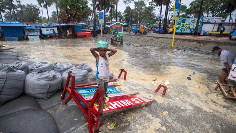 A boy stands on a broken signboard as water flows on to the Kuakata beach on the coast of Bay of Bengal caused by the advancing Cyclone Remal in Barisal, Bangladesh, May 26, 2024.